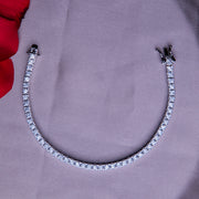 A silver tennis bracelet with a clasp, displayed on a grey surface with a red cloth in the background.
